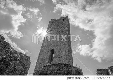 The sun casts a radiant burst of light beside the towering remains of Okor Castle close to Prague, captured in striking monochromatic tones. Czechia. Black and white photography. 113926863