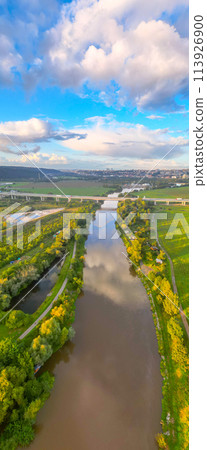 An aerial view of the Lahovice Bridge spanning the Berounka River, surrounded by lush greenery under a cloudy sky. Prague, Czechia An aerial view of the Lahovice Bridge spanning the Berounka River, surrounded by lush greenery under a cloudy sky. Prague, Czechia 113926900