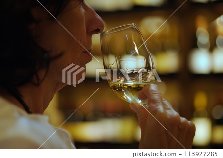 Elegant woman tasting white wine in a warmly lit bar Elegant woman tasting white wine in a warmly lit bar 113927285