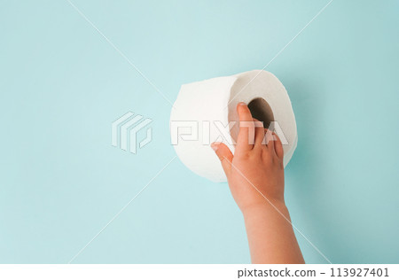 Roll of white toilet paper in child hand. blue background with copy space 113927401