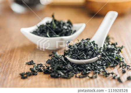 Dried wakame seaweed in spoon on wooden table. 113928526