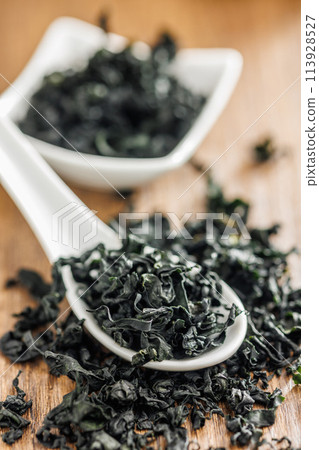 Dried wakame seaweed in spoon on wooden table. 113928527