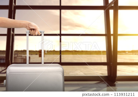 Image of man hand holding soft grey suitcase with airport view on background. Image of man hand holding soft grey suitcase with airport view on background. 113931211