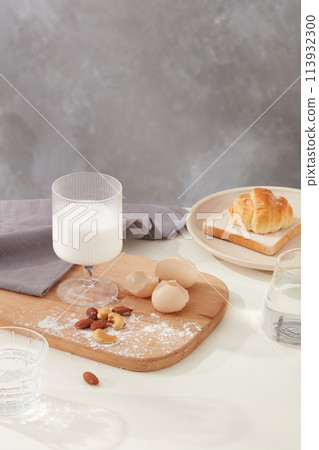 A glasses filled with milk placed on wooden tray, decorated by egg, nuts and gray towel next to a round dish with some cake above and a glass of water. Copy space and blank space for designing A glasses filled with milk placed on wooden tray, decorated by egg, nuts and gray towel next to a round dish with some cake above and a glass of water. Copy space and blank space for designing 113932300
