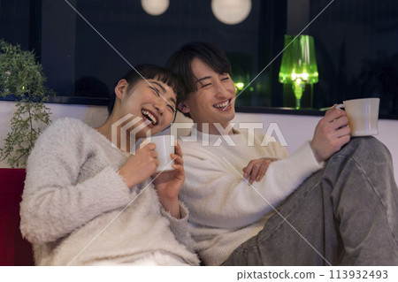 Smiling young man and woman sitting side by side on a sofa 113932493