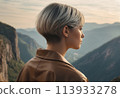 A contemplative woman overlooks mountain scenery at dusk. The peaceful setting reflects her serene and thoughtful mood. 113933278
