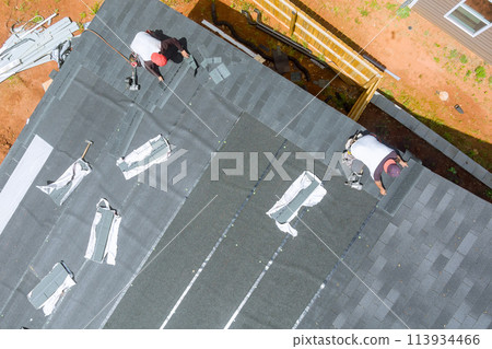 Roofing contractor uses air nail gun to install new asphalt bitumen shingles on roof house Roofing contractor uses air nail gun to install new asphalt bitumen shingles on roof house 113934466