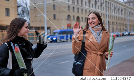 two stylish beautiful young women with flowers in their hands say goodbye 113934577