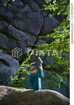 Woman practicing yoga outdoors in forest. Barefoot female on yoga mat surrounded by trees and large rocks, which suggests peaceful, natural environment ideal for meditation or yoga practice. Woman practicing yoga outdoors in forest. Barefoot female on yoga mat surrounded by trees and large rocks, which suggests peaceful, natural environment ideal for meditation or yoga practice. 113935649