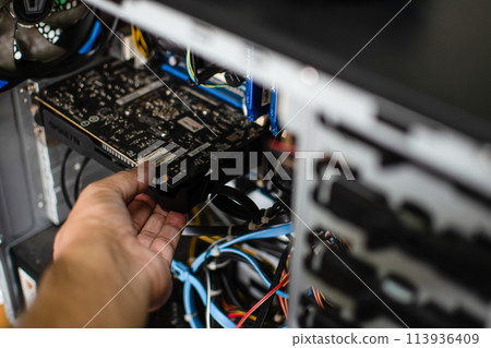 A technician hand holds the graphics card to fix it. The VGA card is damaged causing the computer to fail. Display card does not display a personal computer screen. Take closeup photo. Blur background A technician hand holds the graphics card to fix it. The VGA card is damaged causing the computer to fail. Display card does not display a personal computer screen. Take closeup photo. Blur background 113936409
