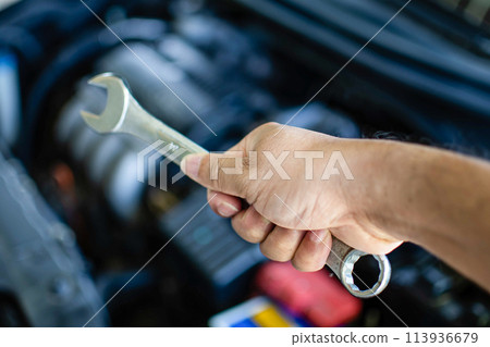 A person is holding a wrench and looking at a car engine A person is holding a wrench and looking at a car engine 113936679