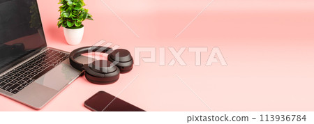 A laptop, a cell phone, and a pair of headphones are on a pink background 113936784