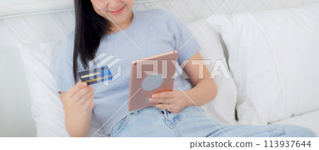 Young asian woman sitting on bed using digital tablet shopping online with credit card. Young asian woman sitting on bed using digital tablet shopping online with credit card. 113937644