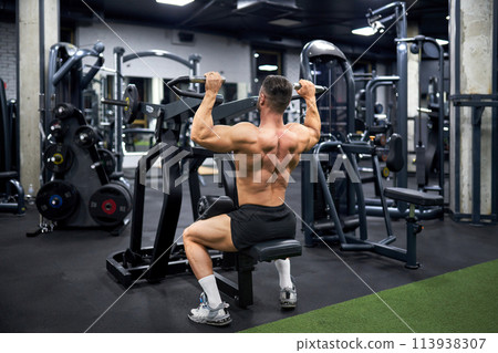 Attractive muscular man doing exercise with training apparatus in sports gym. Back view of strong unrecognizable male athlete with bare torso, building muscles indoors. Sport, bodybuilding concept. 113938307