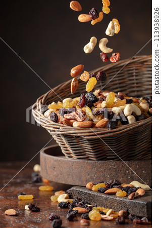 Mix of various nuts and raisins in a old basket on a brown background. 113938926