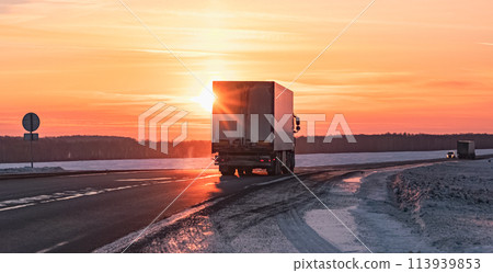 Semi truck driving along a snowy highway at sunset in winter Semi truck driving along a snowy highway at sunset in winter 113939853