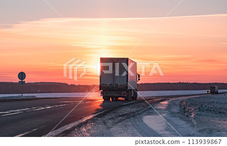 Semi truck driving along a snowy highway at sunset in winter Semi truck driving along a snowy highway at sunset in winter 113939867