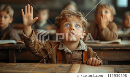 A young boy sits at a desk, eagerly raising his hands as if ready to answer a question during a lesson. 113939898