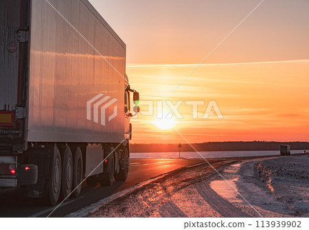 Semi truck driving along a snowy highway at sunset in winter 113939902