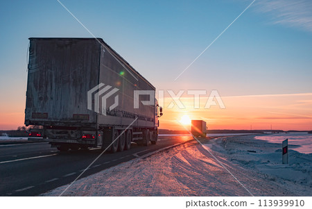 Semi truck driving along a snowy highway at sunset in winter 113939910