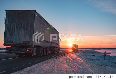 Semi truck driving along a snowy highway at sunset in winter 113939912
