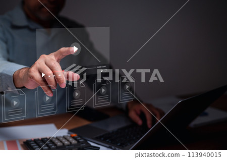 A man is pointing at a laptop screen with a video player icon 113940015