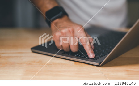 A man is pointing at a laptop on a wooden table 113940149