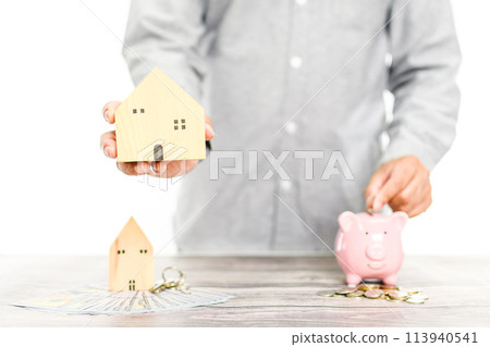 A man is holding a house model and a piggy bank A man is holding a house model and a piggy bank 113940541