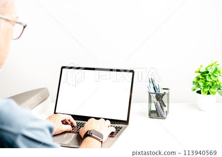 A man is typing on a laptop with a white screen 113940569