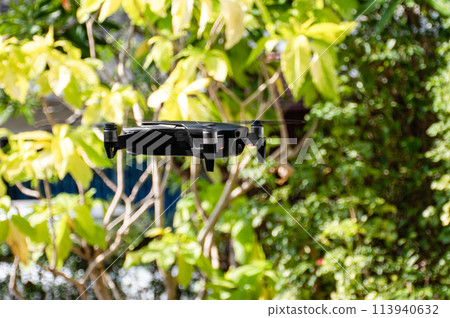 A black drone is flying over a lush green forest A black drone is flying over a lush green forest 113940632