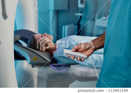 Unrecognizable radiographer holding controller turning on MRI scanner for mature Caucasian female patient, copy space 113941199