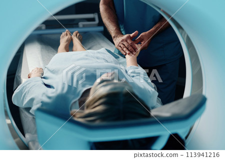 Selective focus shot of unrecognizable doctor holding hand of mature Caucasian woman before CT scan procedure in modern clinic 113941216