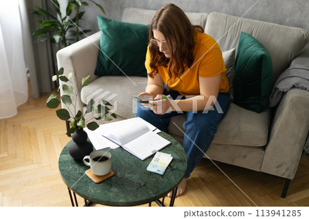 The 30s woman considers the costs of gas, electricity, heating. The concept of increasing tariffs for services. Woman with financial bills calculating on smart phone. Debt, bankruptcy The 30s woman considers the costs of gas, electricity, heating. The concept of increasing tariffs for services. Woman with financial bills calculating on smart phone. Debt, bankruptcy 113941285