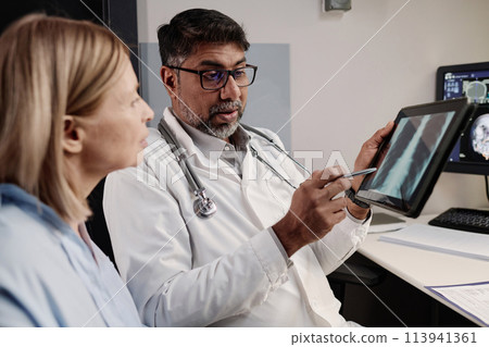 Biracial professional radiographer showing chest X-ray image on digital tablet screen to mature Caucasian female patient, copy space Biracial professional radiographer showing chest X-ray image on digital tablet screen to mature Caucasian female patient, copy space 113941361