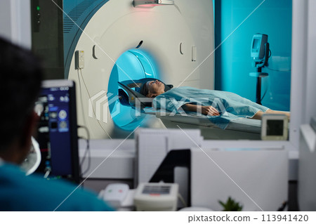 Selective focus shot of mature Caucasian woman having CT scan procedure in modern clinic, unrecognizable doctor looking at computer monitor Selective focus shot of mature Caucasian woman having CT scan procedure in modern clinic, unrecognizable doctor looking at computer monitor 113941420