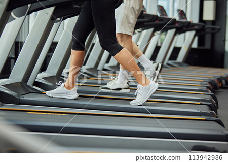 Cardio training to fat burning. Cropped portrait of senior man's and woman's legs on treadmill in fitness center. 113942986