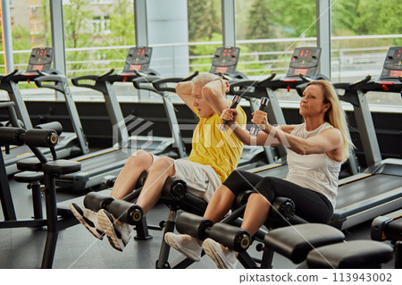 Active aging couple doing abdominal exercises together in modern fitness center, man and woman looks focused. Active aging couple doing abdominal exercises together in modern fitness center, man and woman looks focused. 113943002