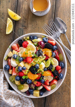 Fruit salad on a wooden table with berries and honey dressing 113943111