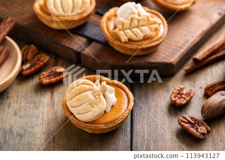 Mini pumpkin pies for Thanksgiving with leaves and pumpkin garnishes and whipped cream Mini pumpkin pies for Thanksgiving with leaves and pumpkin garnishes and whipped cream 113943127