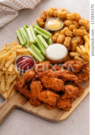 Fried chicken strips and french fries board with sauces and celery Fried chicken strips and french fries board with sauces and celery 113943370