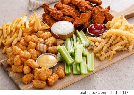Fried chicken strips and french fries board with sauces and celery 113943371