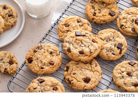 Chocolate chip cookies on a cooling rack with flaky salt served with milk 113943378