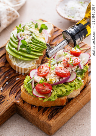 Avocado toasts with radishes, tomatoes and feta topped with olive oil Avocado toasts with radishes, tomatoes and feta topped with olive oil 113943397