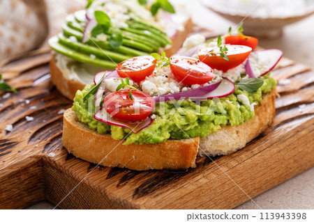 Avocado toasts with radishes, tomatoes and feta topped with olive oil Avocado toasts with radishes, tomatoes and feta topped with olive oil 113943398