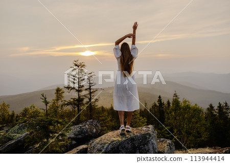 Woman standing on mountain top with raised arms 113944414