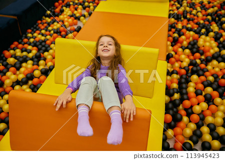 Happy excited girl child crawling in pool with balls at recreation center 113945423