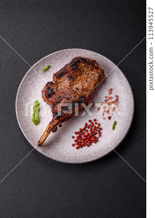 Delicious juicy beef steak on the bone, tomahawk with salt, spices and herbs Delicious juicy beef steak on the bone, tomahawk with salt, spices and herbs 113945527