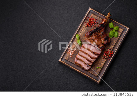 Delicious juicy beef steak on the bone, tomahawk with salt, spices and herbs Delicious juicy beef steak on the bone, tomahawk with salt, spices and herbs 113945532
