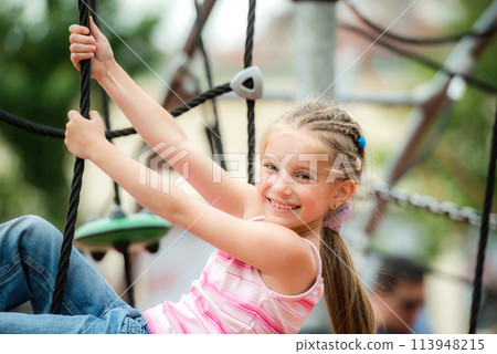 portrait of cute smiling little girl playing at the playground and climb the ropes outdoor portrait of cute smiling little girl playing at the playground and climb the ropes outdoor 113948215