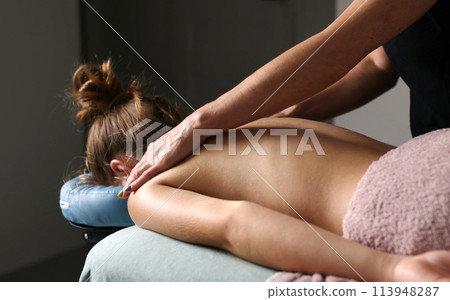 Professional Masseuse Massaging Back And Shoulder Blades Of Young Woman Lying On A Massage Table. Professional Masseuse Massaging Back And Shoulder Blades Of Young Woman Lying On A Massage Table. 113948287